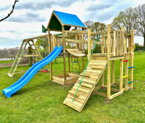 Large wooden climbing frame with slide, climbing wall, clatter bridge and swings on a grassy lawn