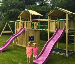 Wooden climbing frame with two slides, climbing net, net bridge and swings in a garden